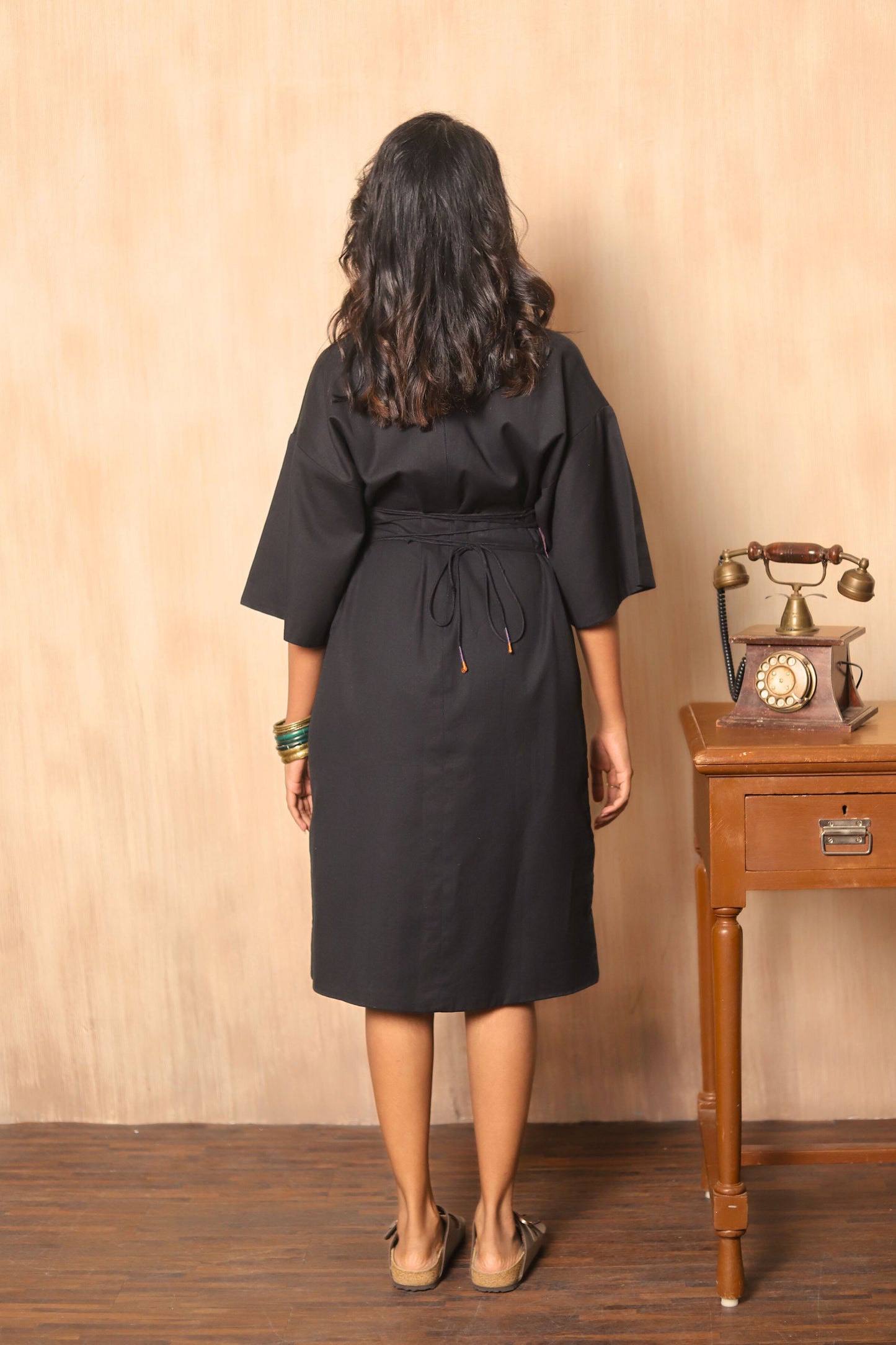 Woman wearing a black dress standing in front of a wooden table with a vintage phone.