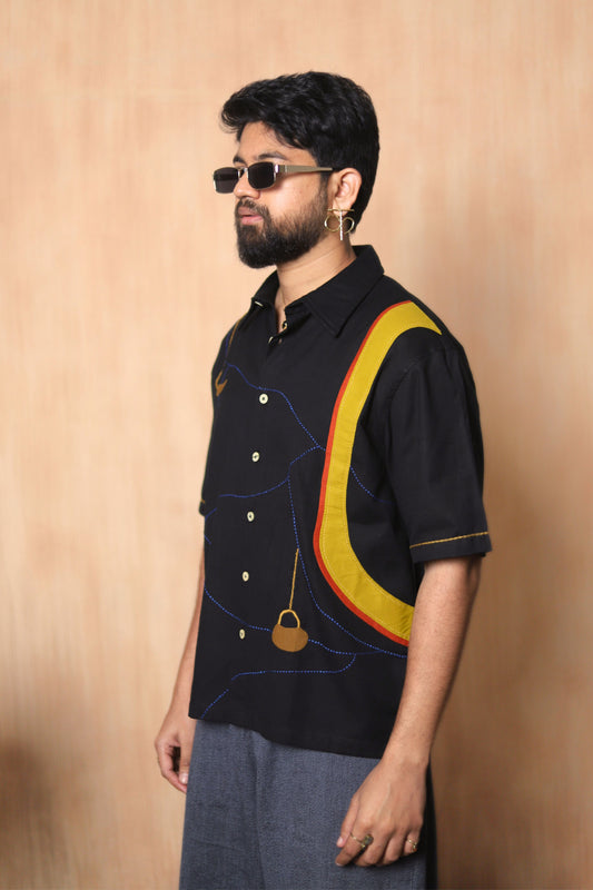 Man wearing a black shirt with yellow and red design against a beige background