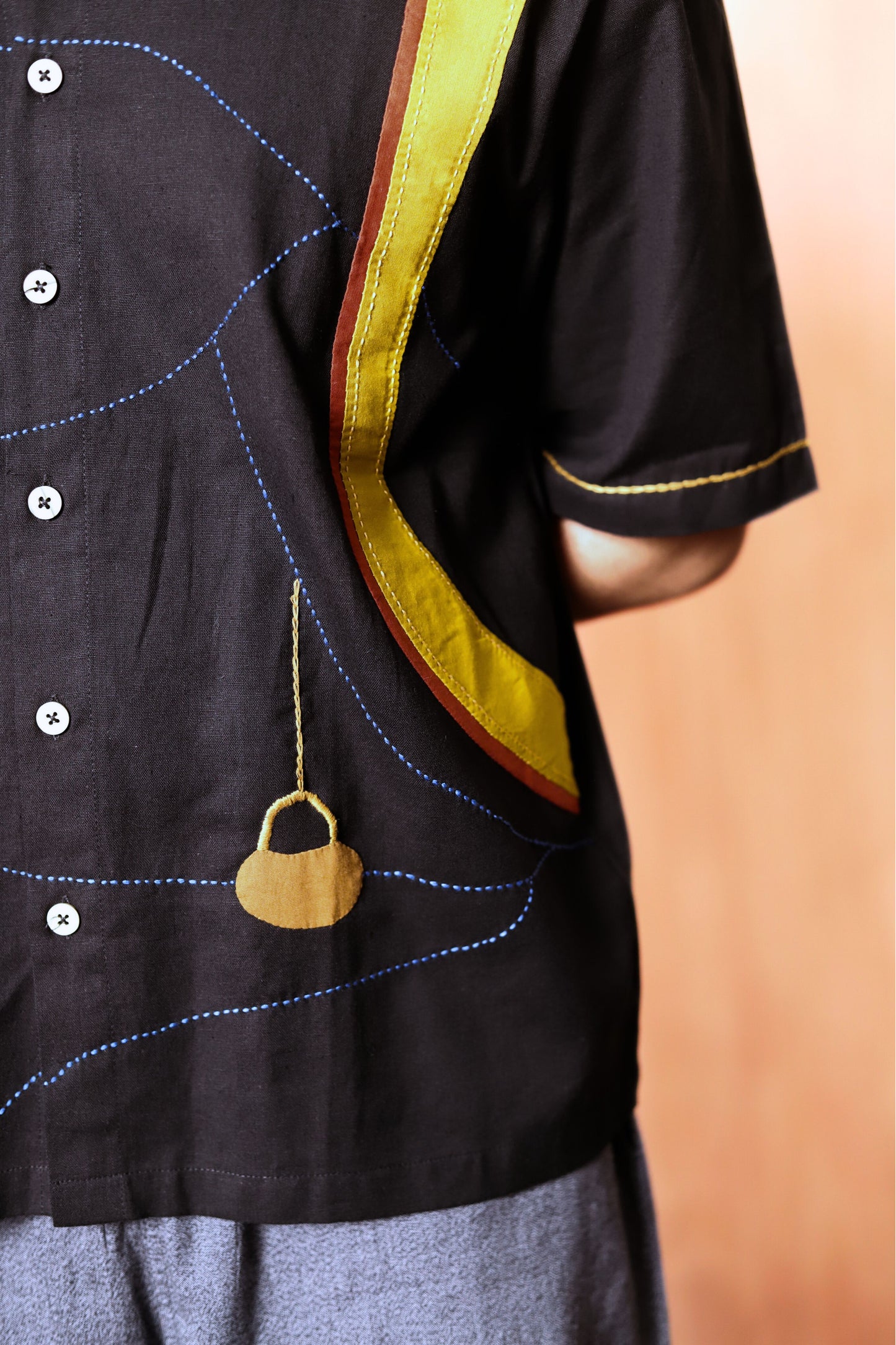 Black shirt with yellow trim and a decorative pendant on a blurred background