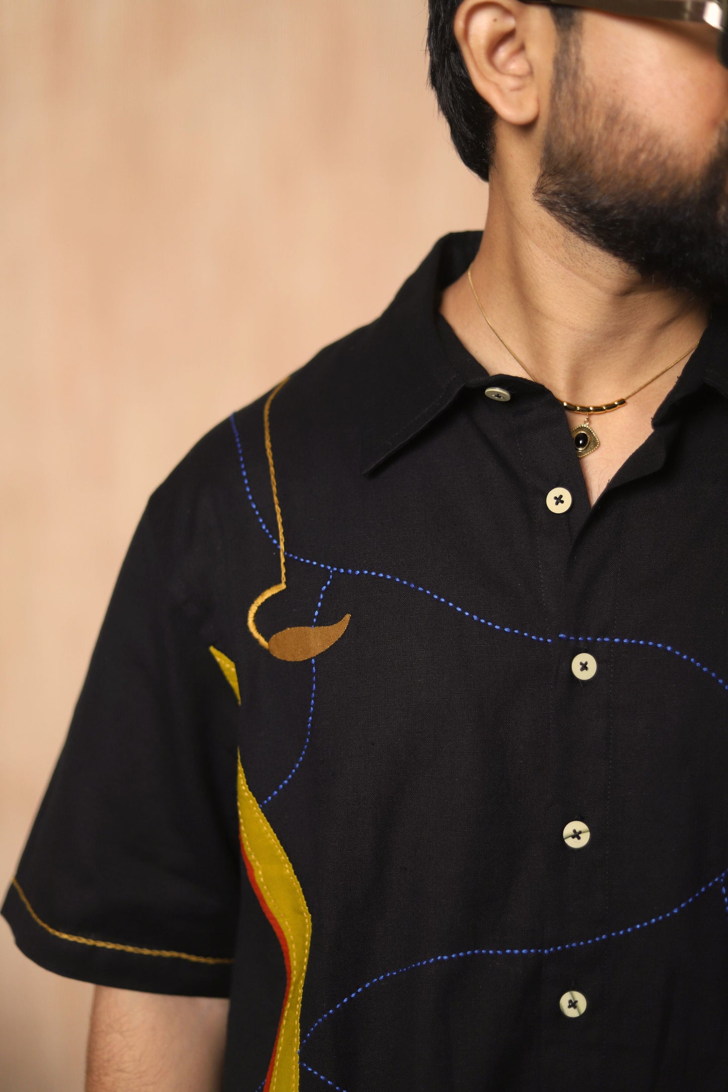Man wearing a black shirt with colorful embroidery on a beige background