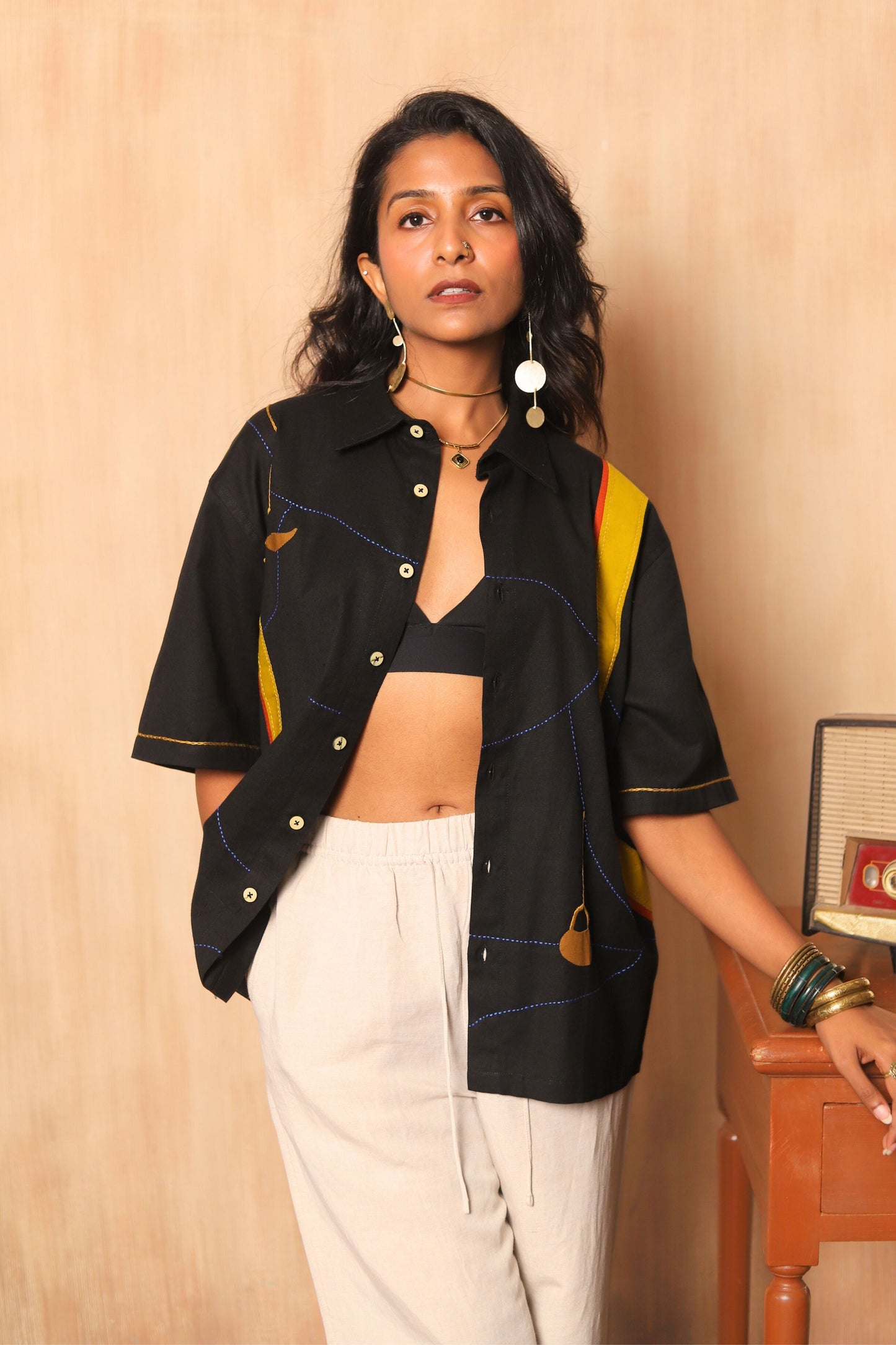 Woman wearing a black and yellow top with white pants against a beige wall.