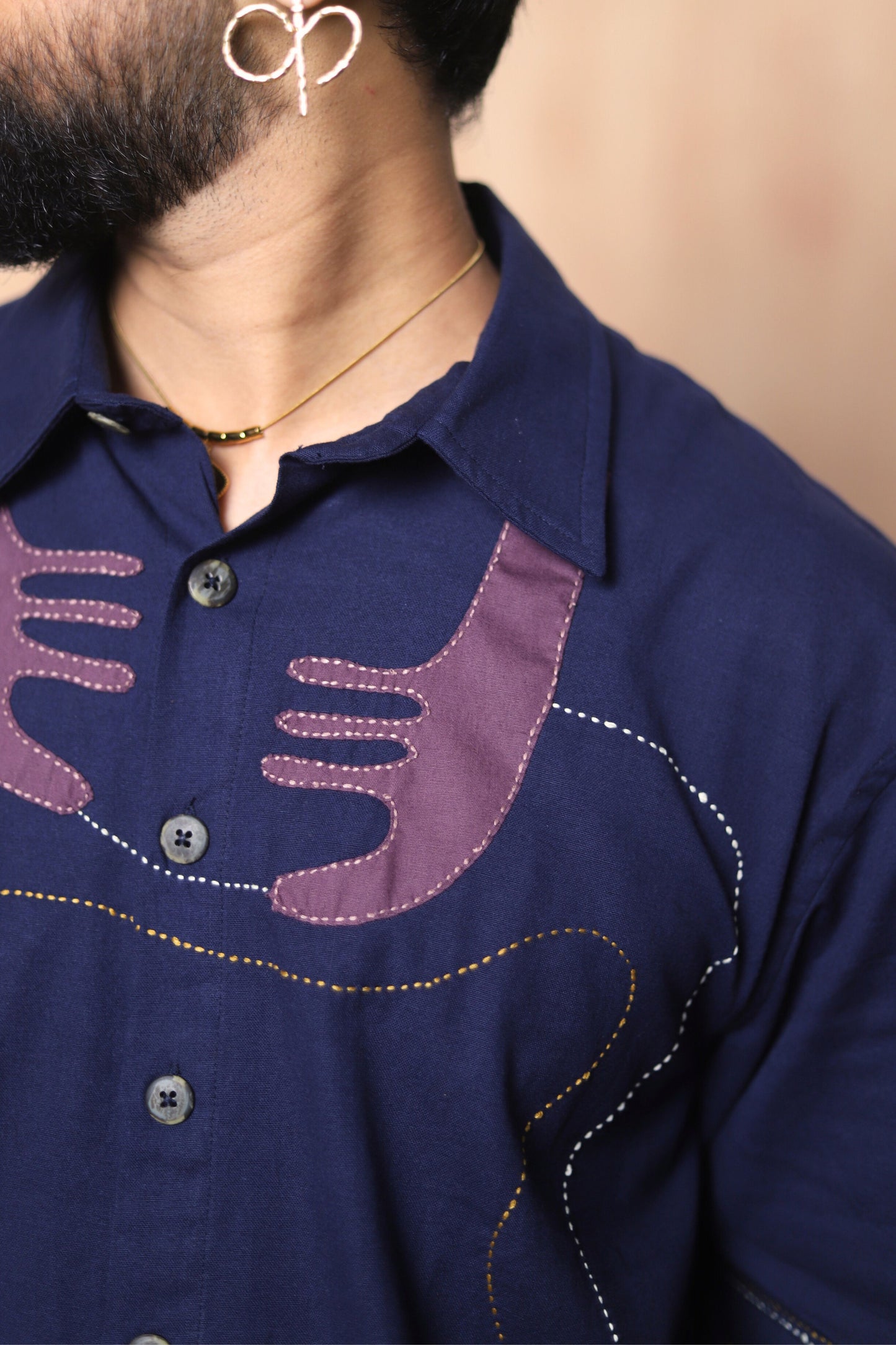 Navy blue shirt with purple embroidered design on a beige background