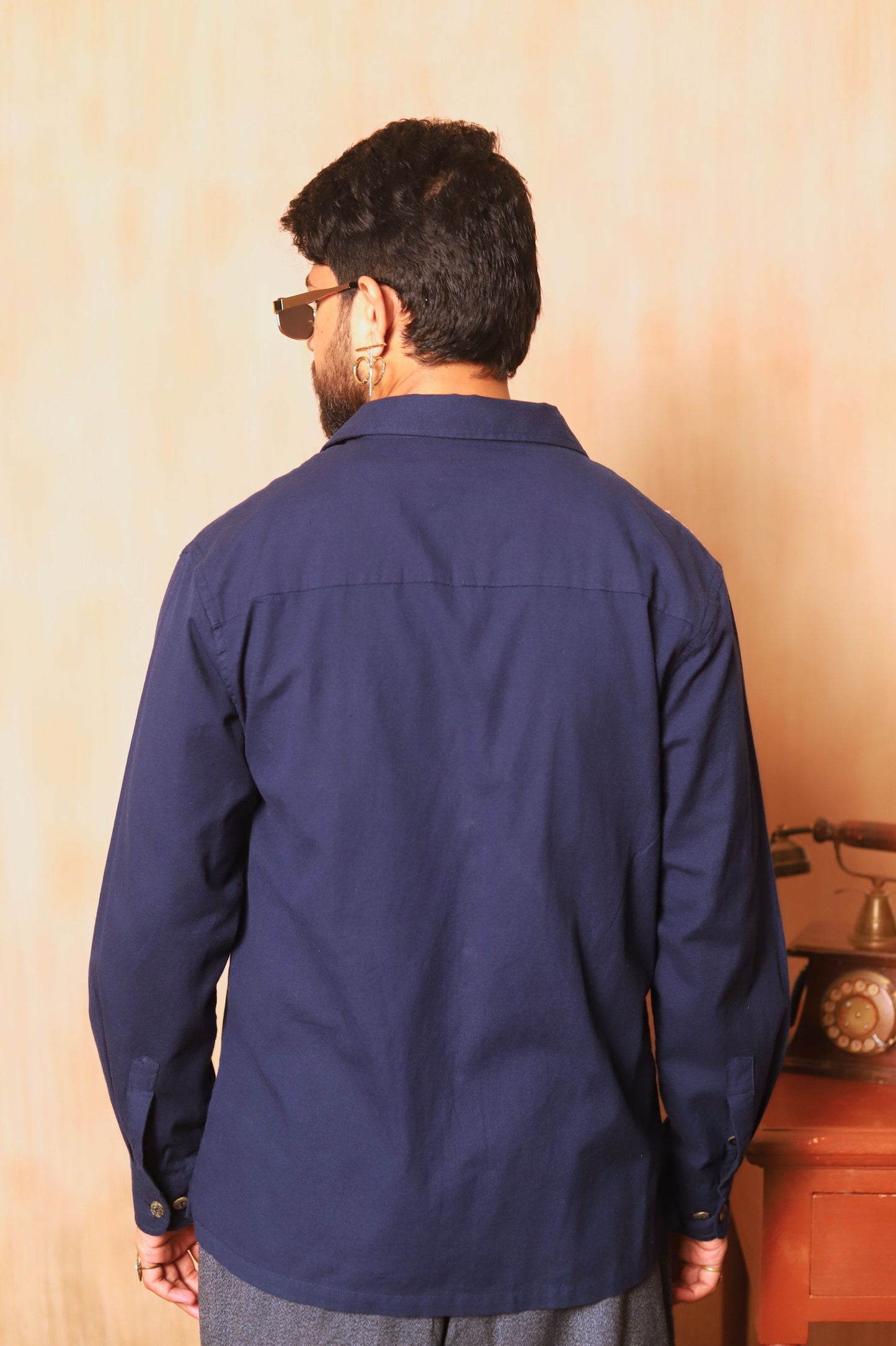 Man wearing a navy blue shirt from behind with a beige wall background