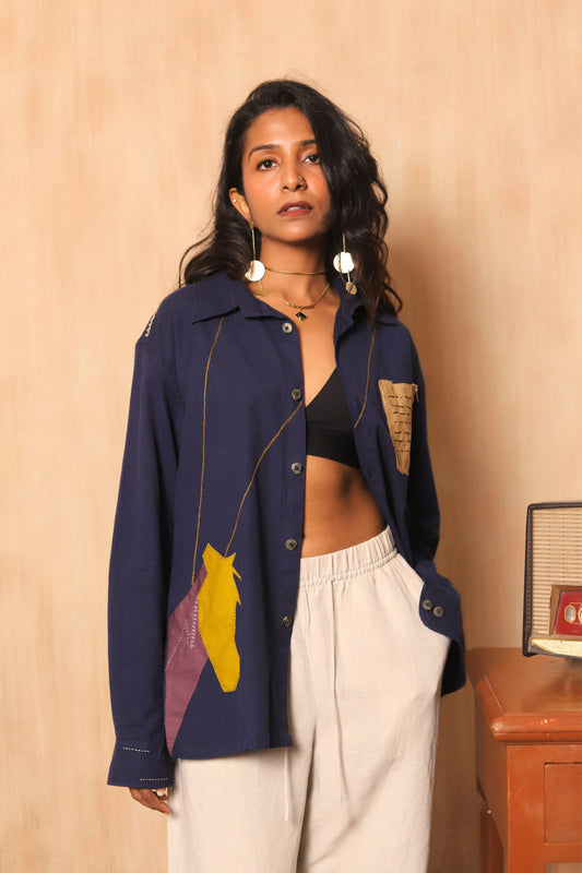 Woman wearing a navy blue jacket with colorful patches against a beige wall.