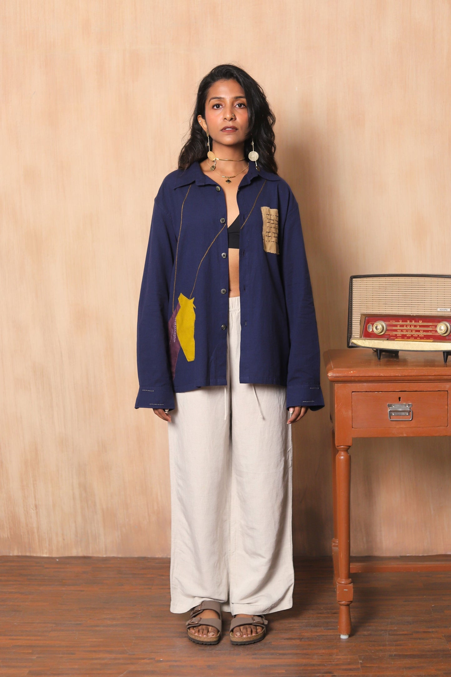 Woman wearing a blue jacket with a yellow design in a room with wooden furniture.