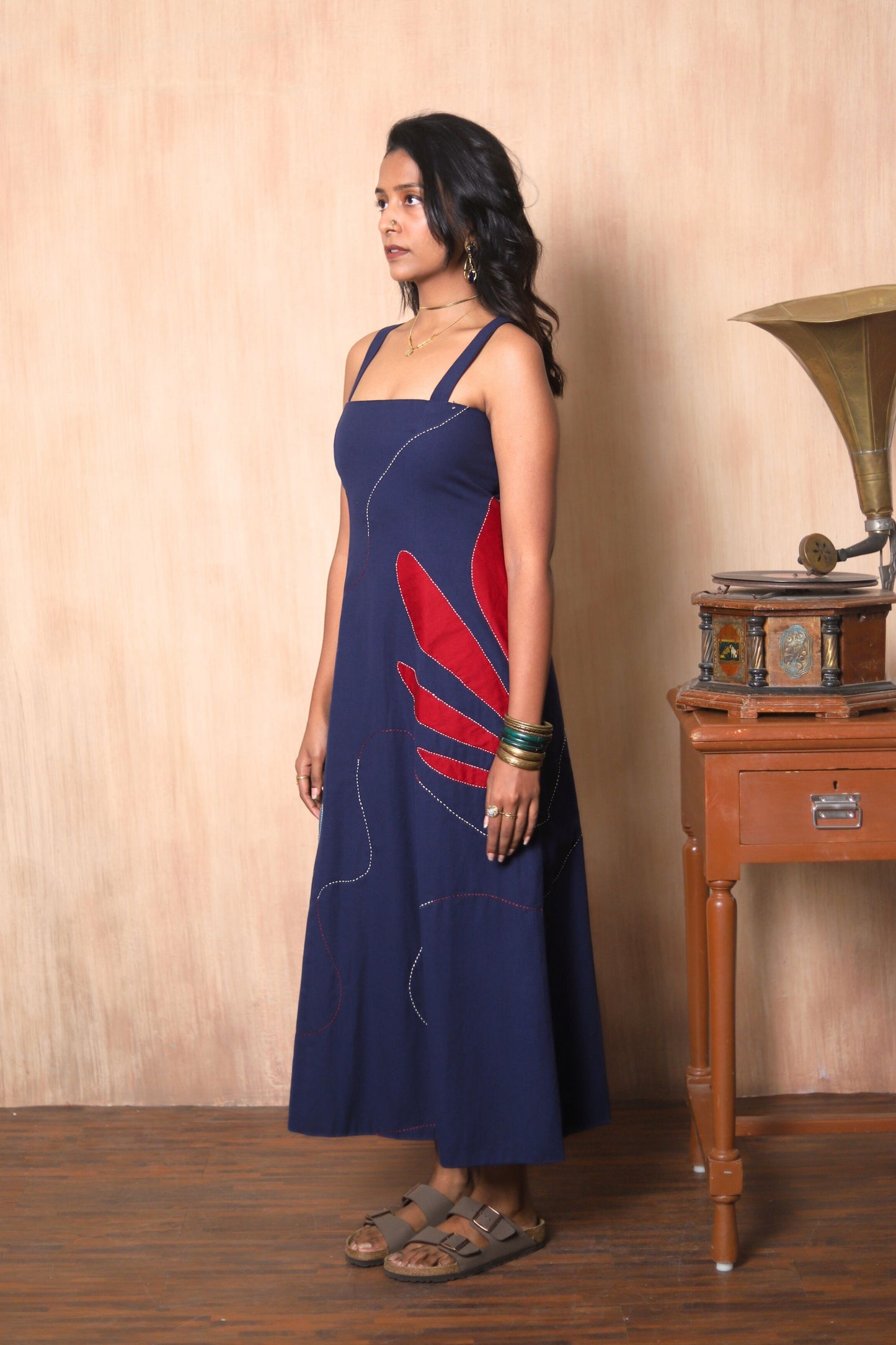 Woman in a blue dress with red design standing next to a vintage gramophone.