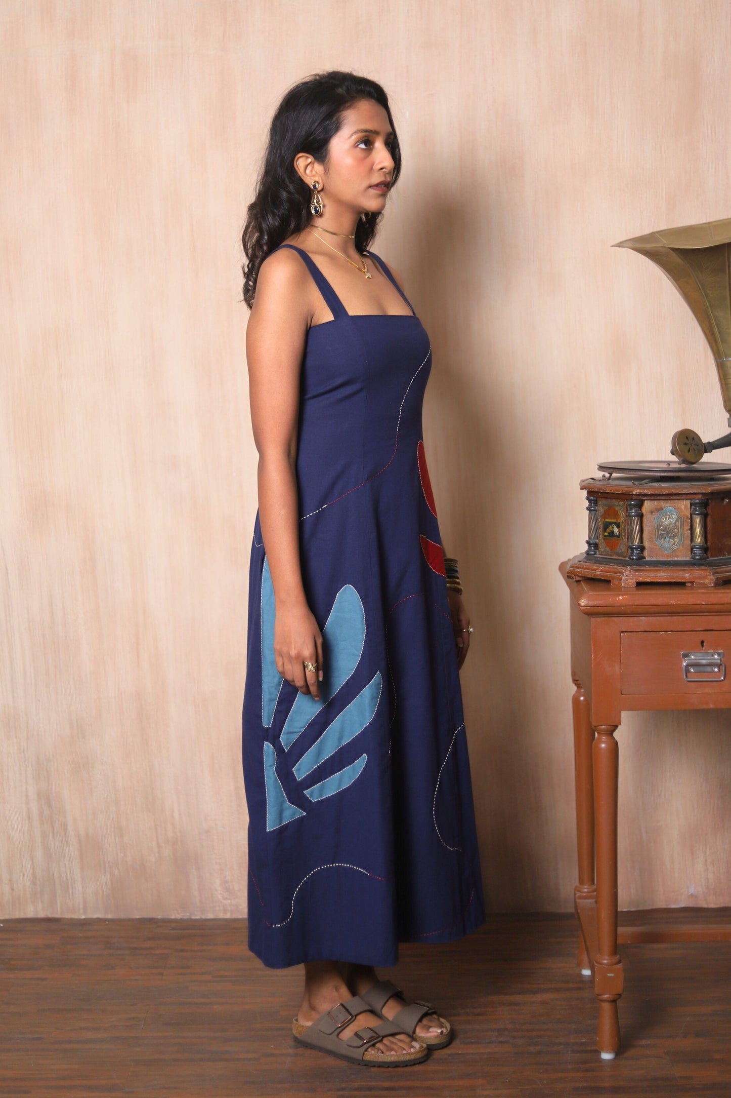 Woman in a navy blue dress with a blue design standing next to a wooden side table with a vintage record player.