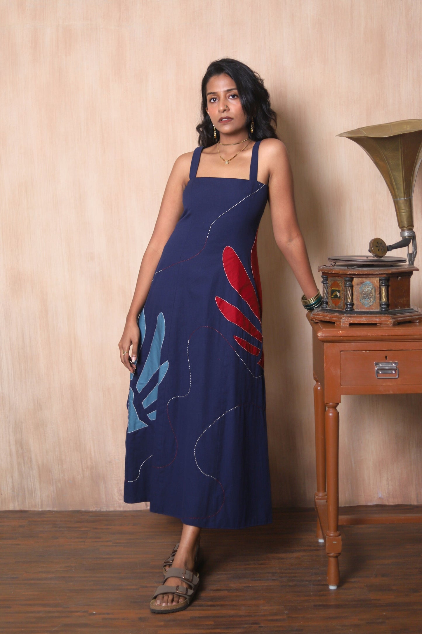 Woman in a blue dress with red and blue abstract designs standing next to a vintage record player.