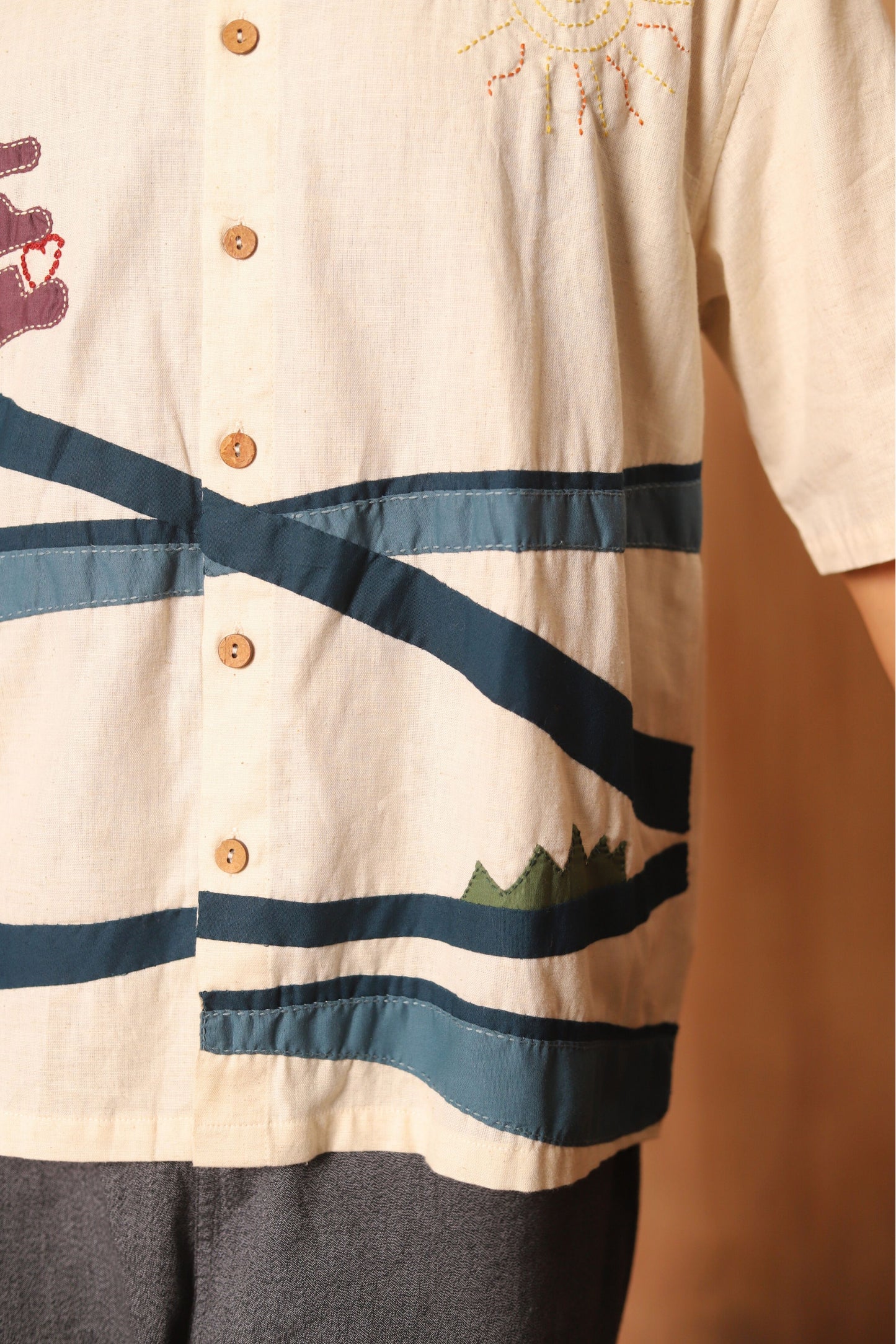 Close-up of a person wearing a beige shirt with blue stripes and embroidery details.
