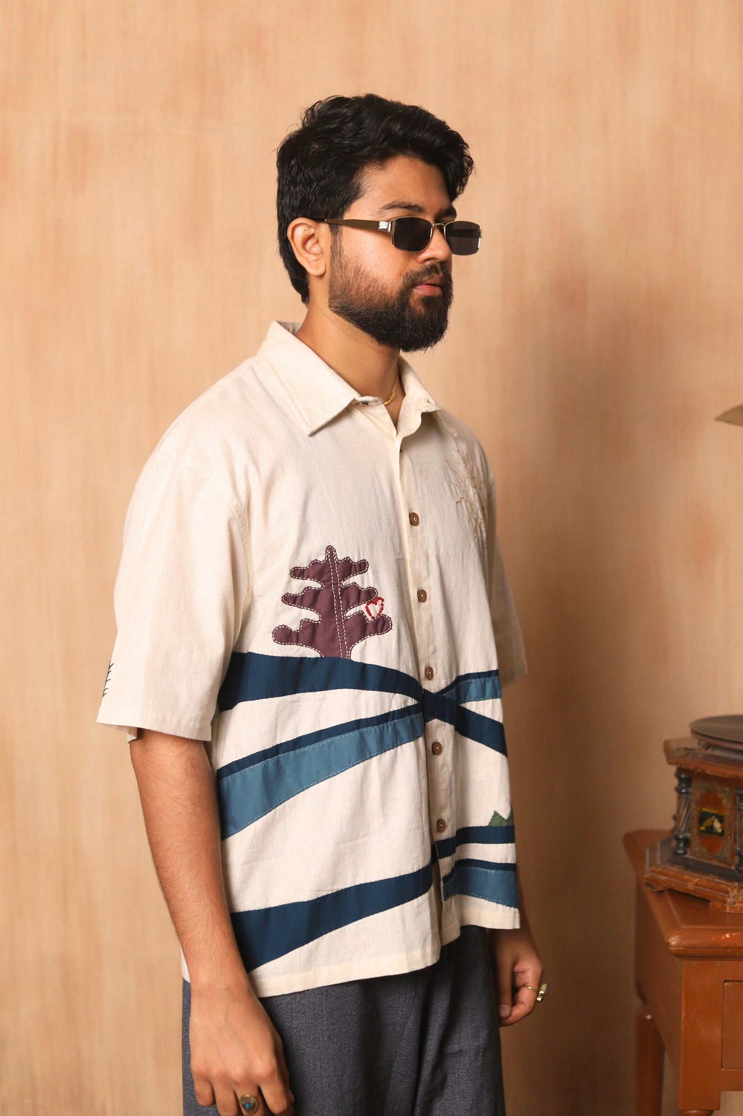 Man wearing a white shirt with blue stripes and a graphic design, standing against a beige wall.