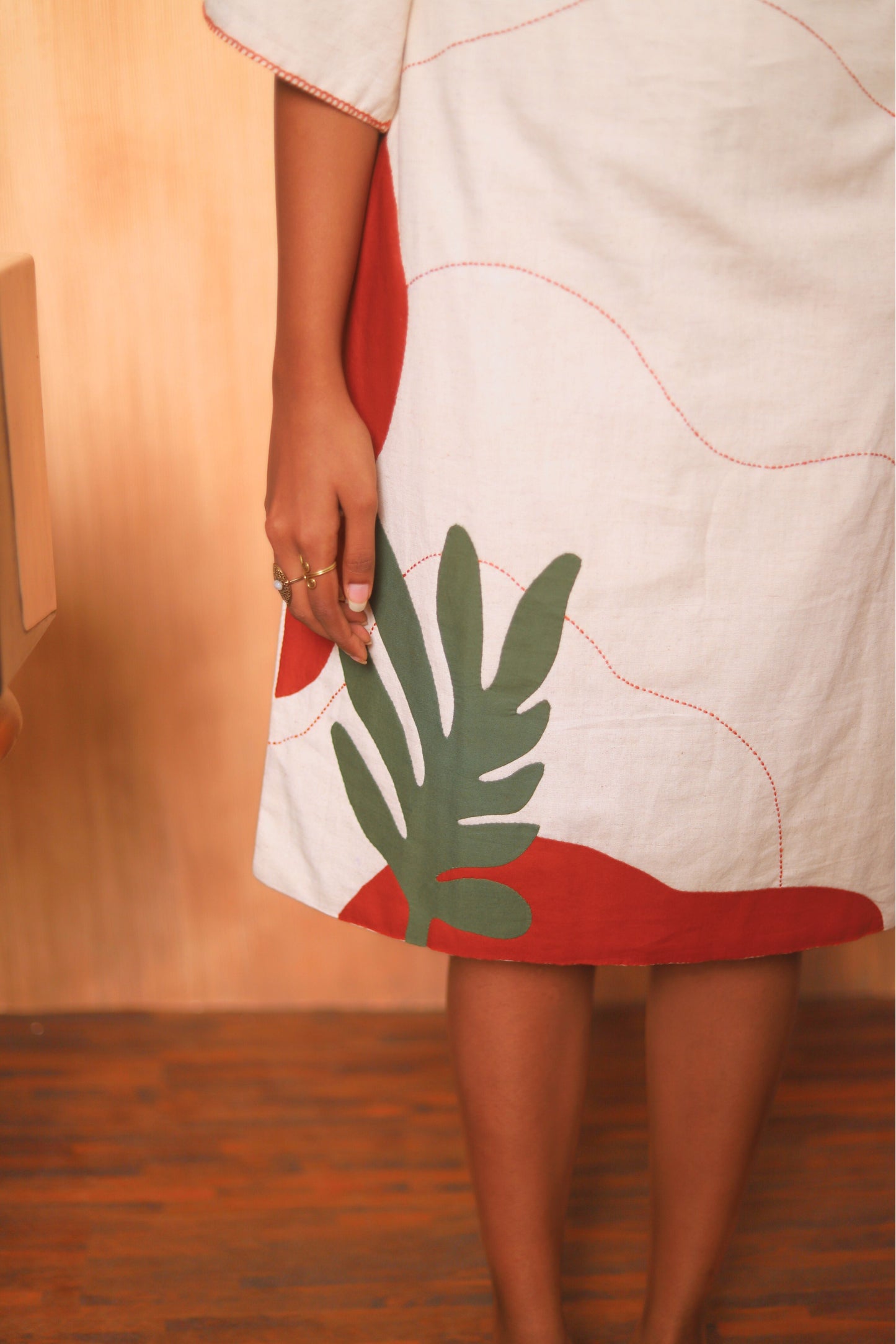 Person wearing a white dress with red accents and a green leaf design.