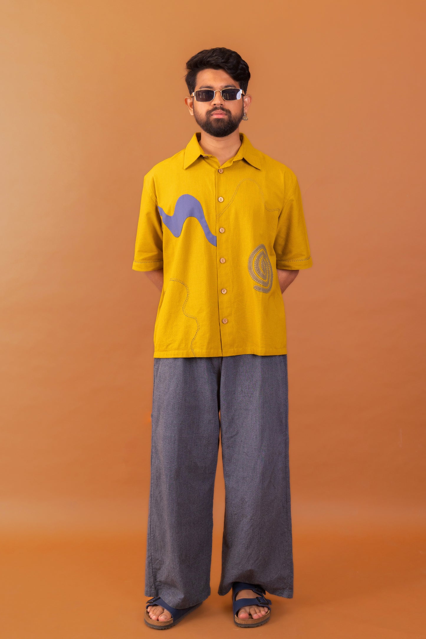 Man wearing a yellow shirt with graphic designs on an orange background