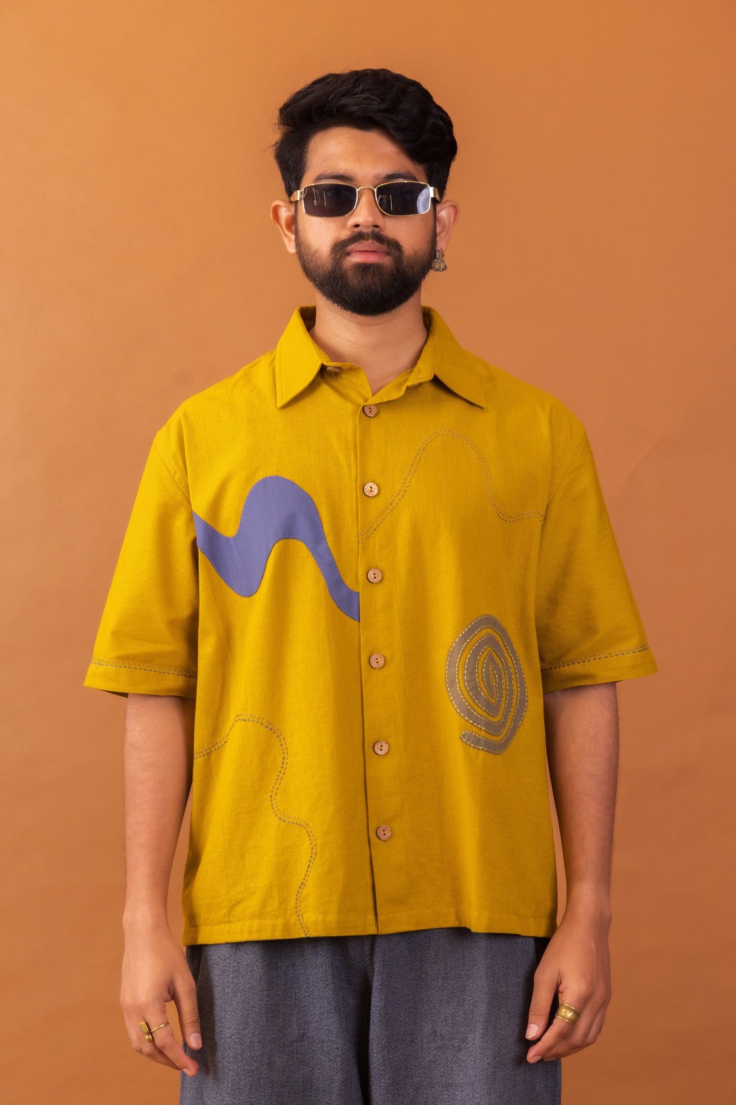 Man wearing a mustard yellow shirt with graphic designs on an orange background