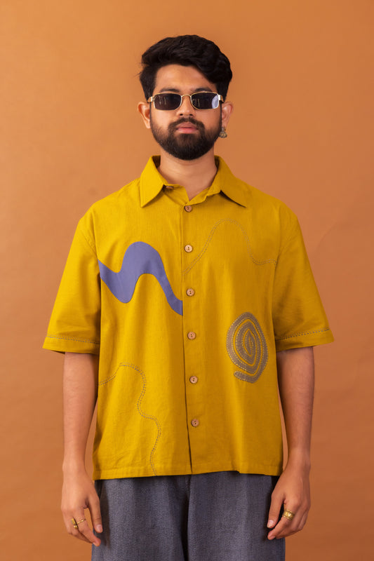 Man wearing a mustard yellow shirt with graphic designs on an orange background