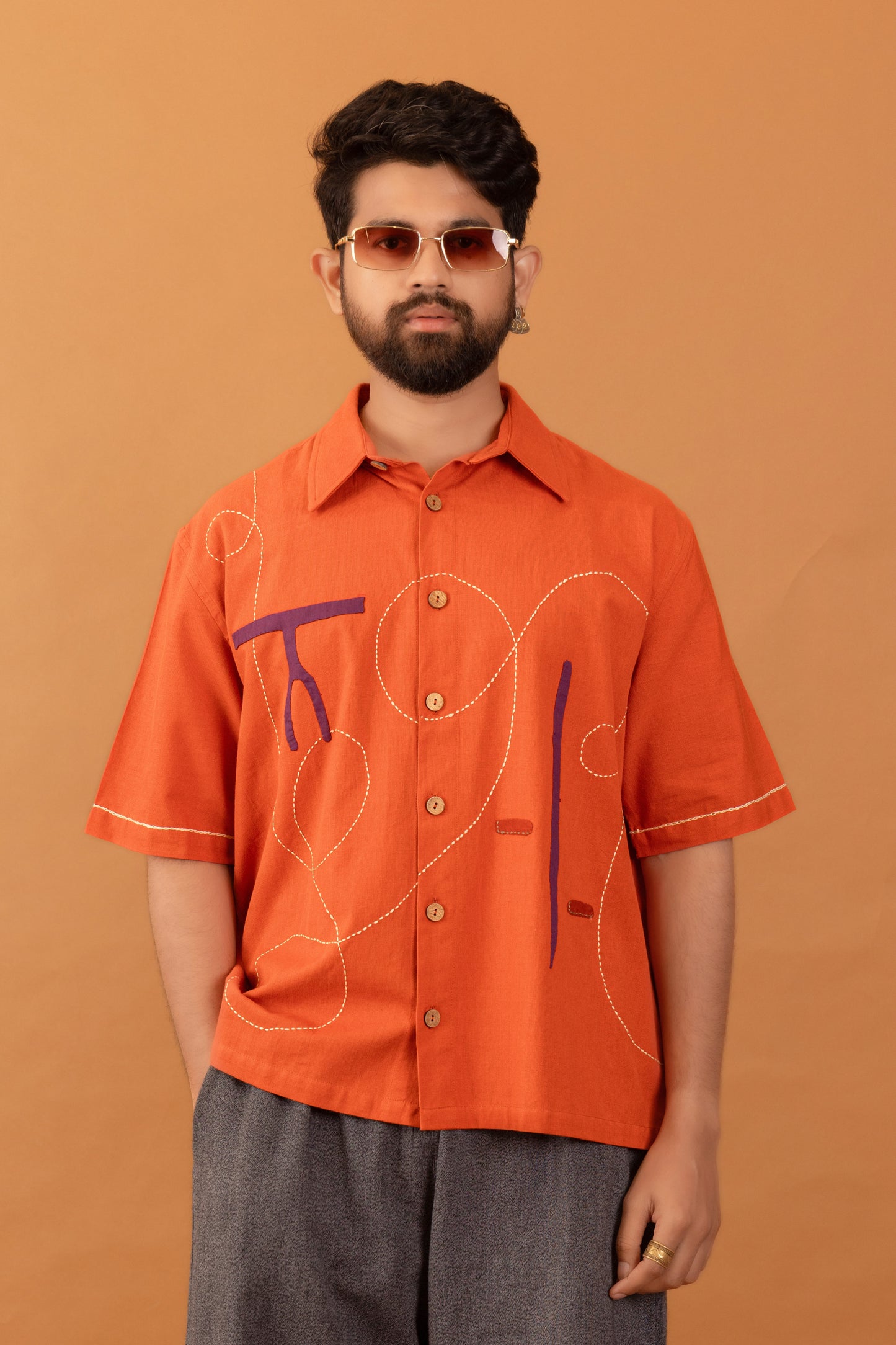 Man wearing an orange shirt with abstract designs on a brown background