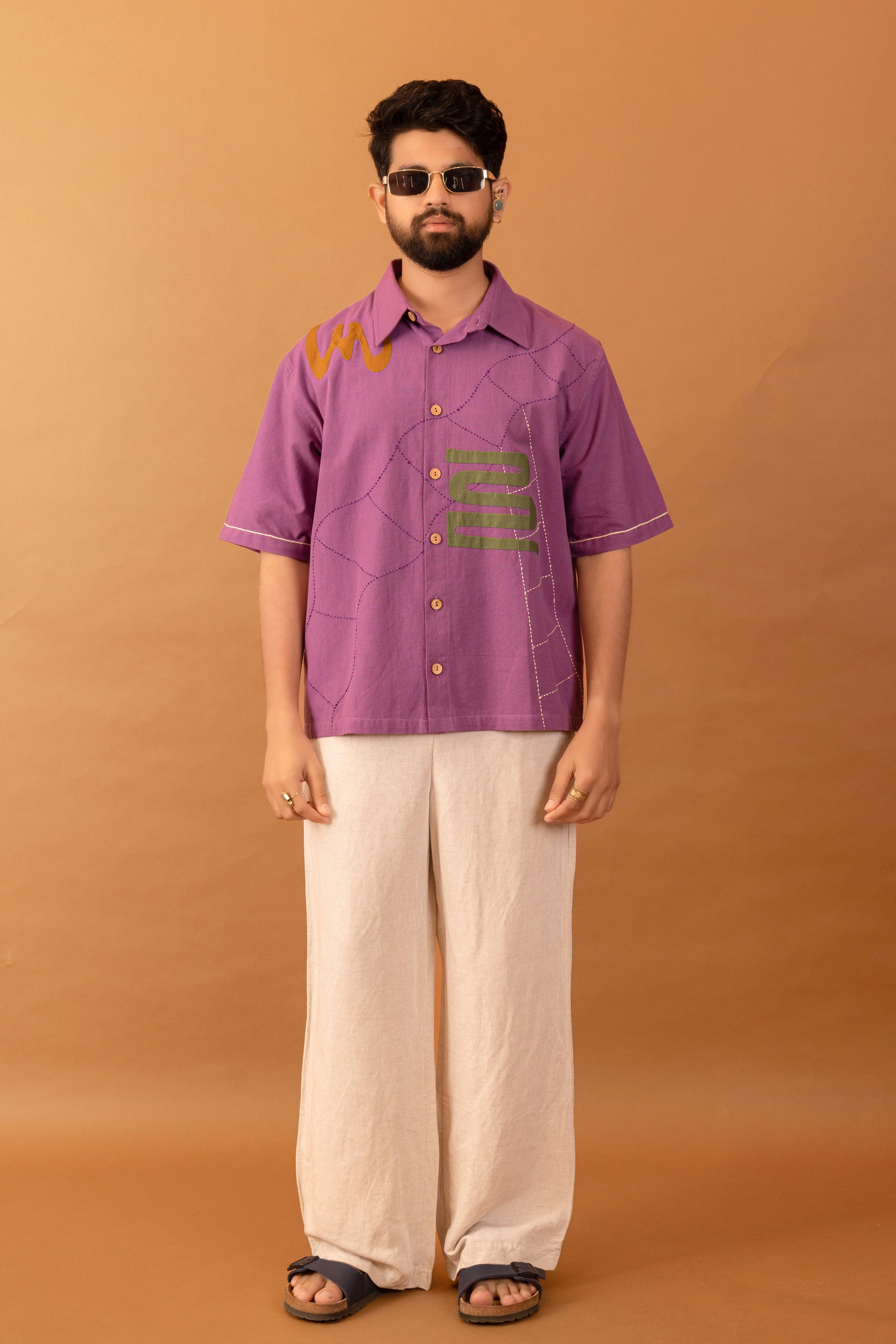 Man wearing a purple shirt with text and white pants against an orange background