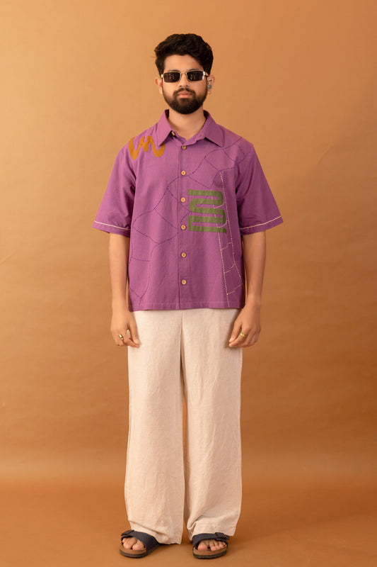 Man wearing a purple shirt with text and white pants against an orange background