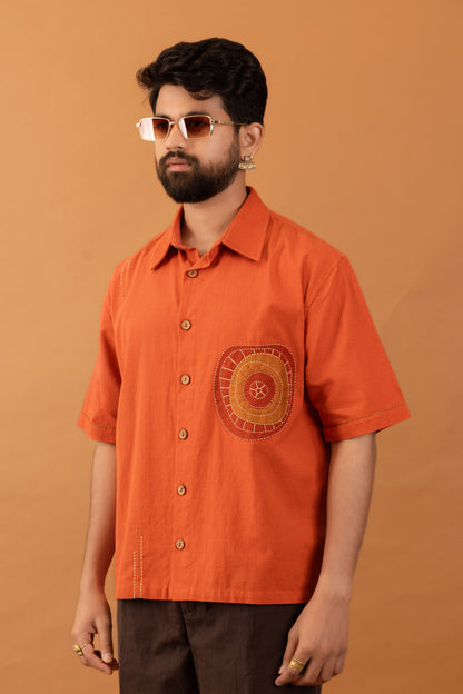 Man wearing an orange shirt with a decorative patch against a brown background