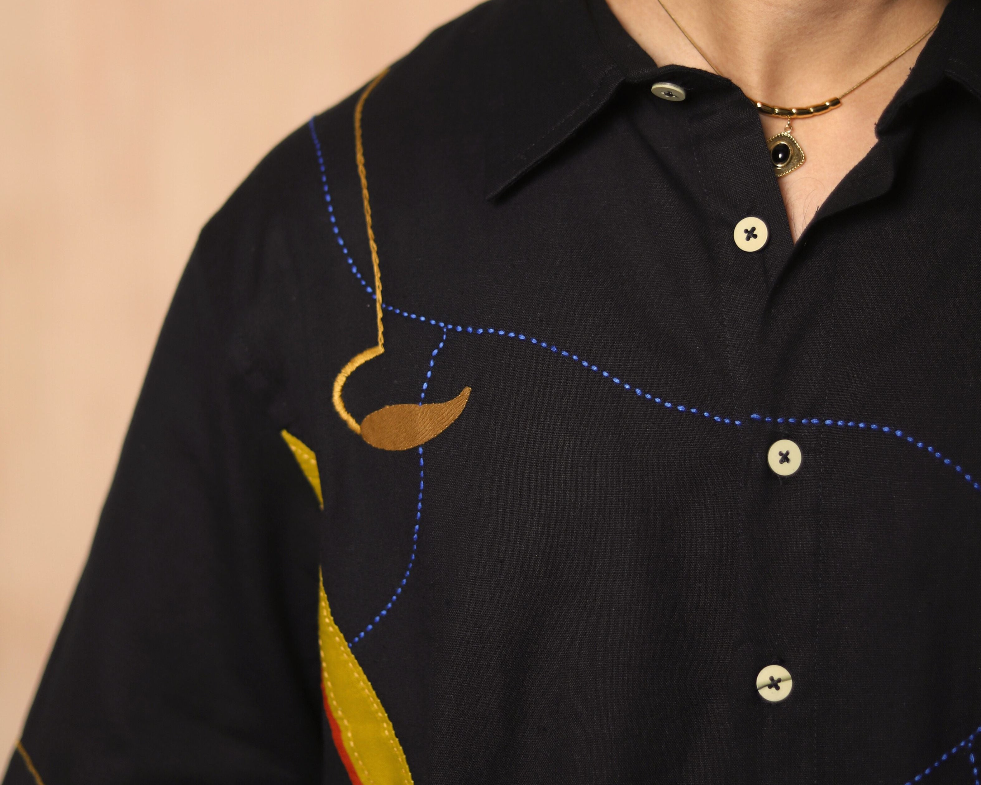 Man wearing a black shirt with colorful embroidery on a beige background