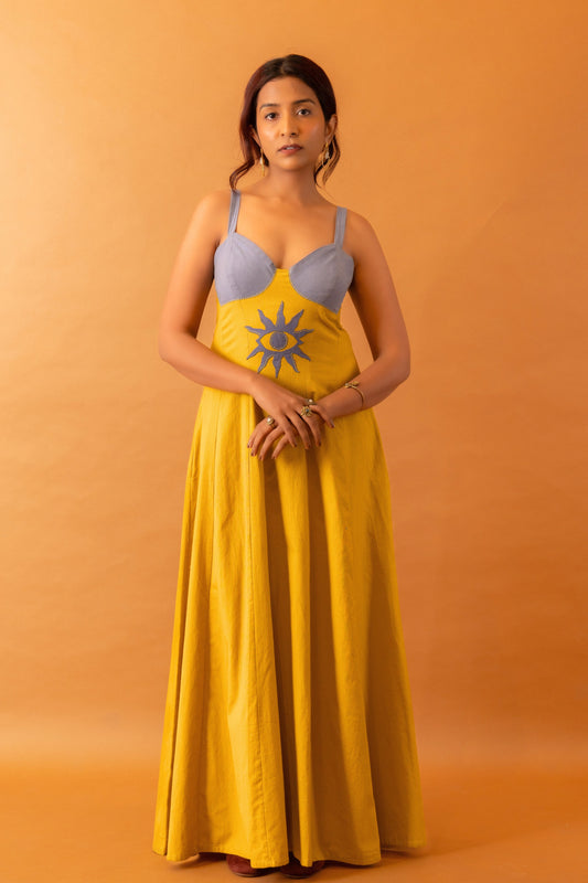 Woman wearing a yellow dress with a blue bralette against an orange background