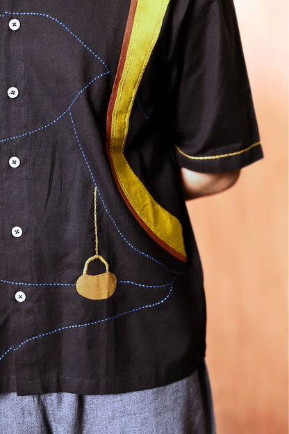 Black shirt with yellow trim and a decorative pendant on a blurred background