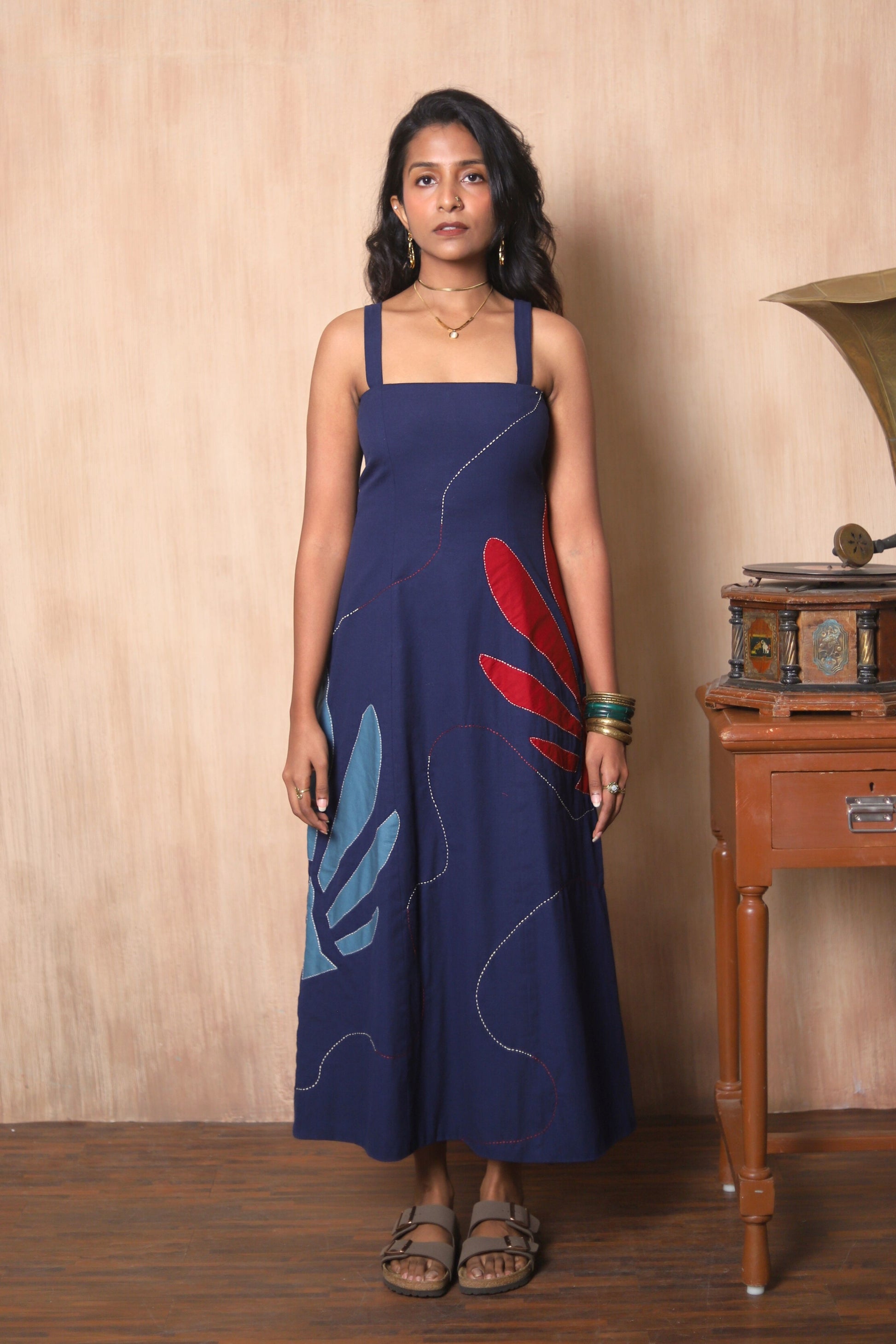 Woman wearing a blue dress with red and blue floral patterns in a room with wooden furniture.