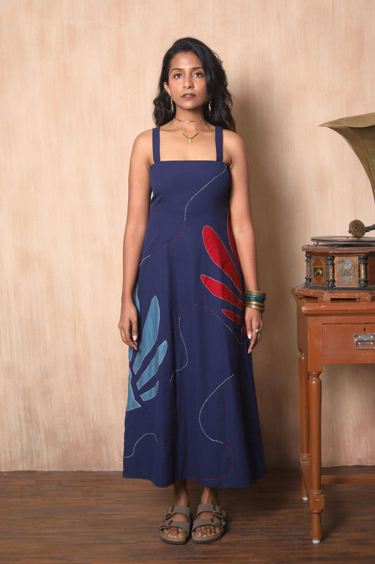 Woman wearing a blue dress with red and blue floral patterns in a room with wooden furniture.