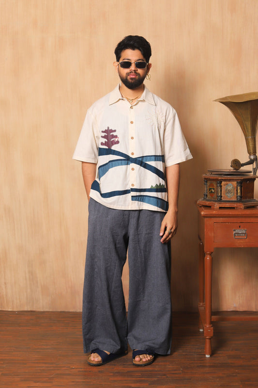 Man wearing a patterned shirt and sunglasses standing next to a vintage gramophone against a wooden wall.